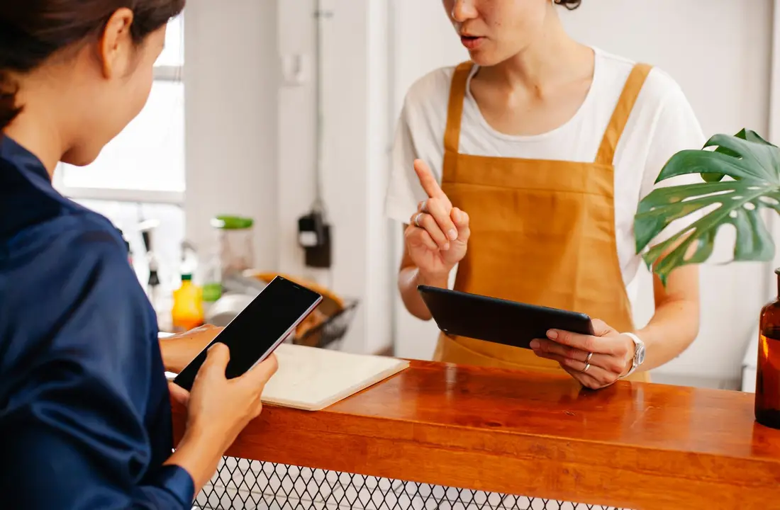 Crop anonymous female employee with finger up speaking with partner touching black screen on cellphone in cafe