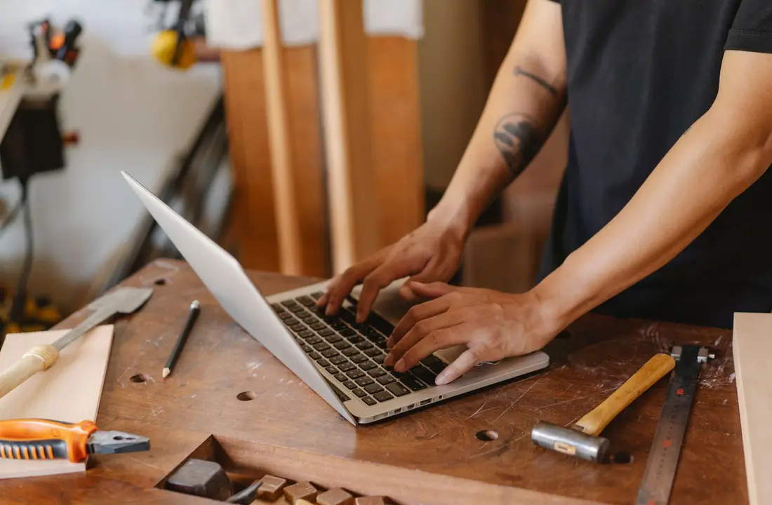 From above of crop anonymous male joiner with tattoo surfing internet on netbook in workshop