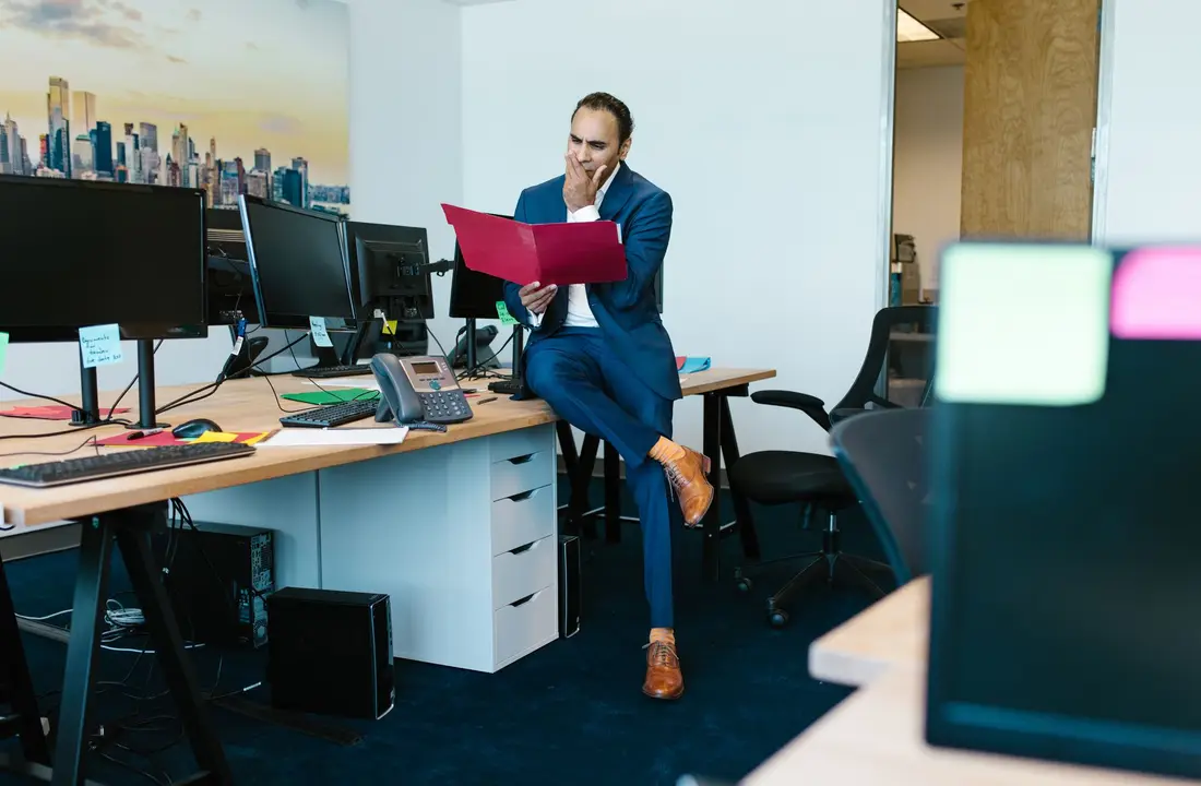 A thoughtful businessman examines documents in a modern office setting.