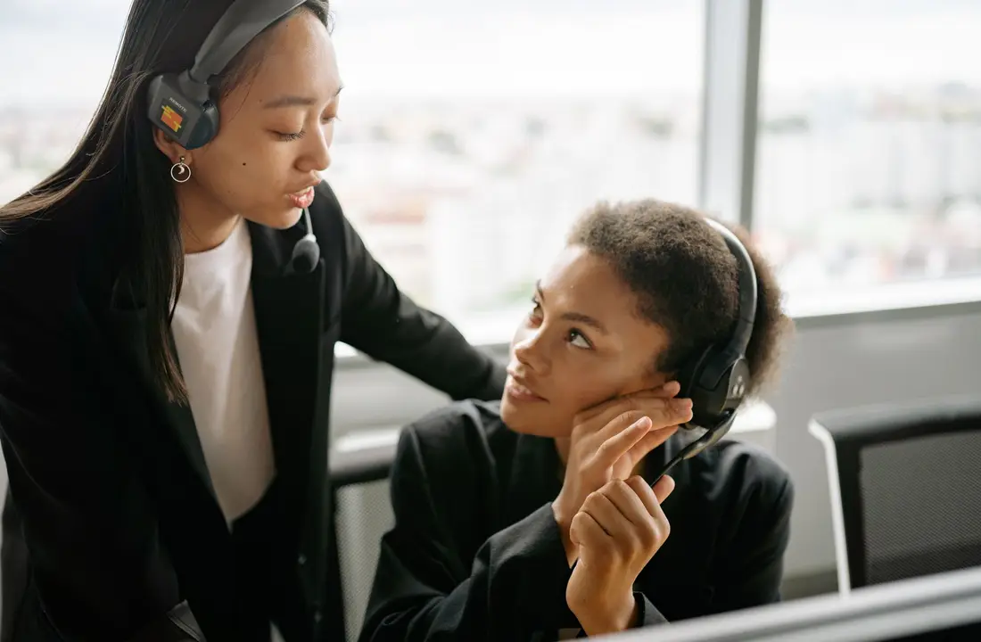 Two call center agents discussing strategies with headsets in a modern office setting.