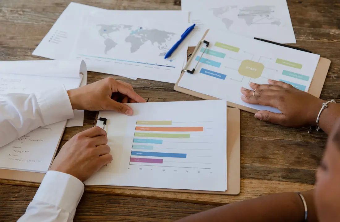 Top view of colleagues discussing charts and graphs on a wooden table during a business meeting.