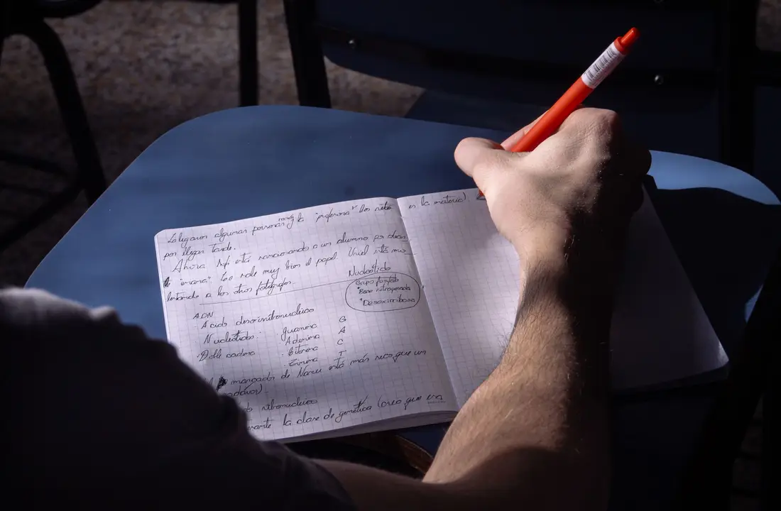 A student takes notes in a classroom in Buenos Aires. Natural lighting highlights the writing process.