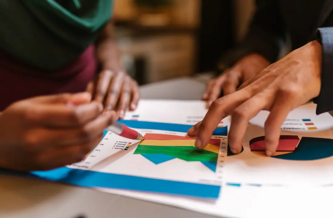 Close-up of hands during a collaborative office meeting analyzing colorful graphs and documents.