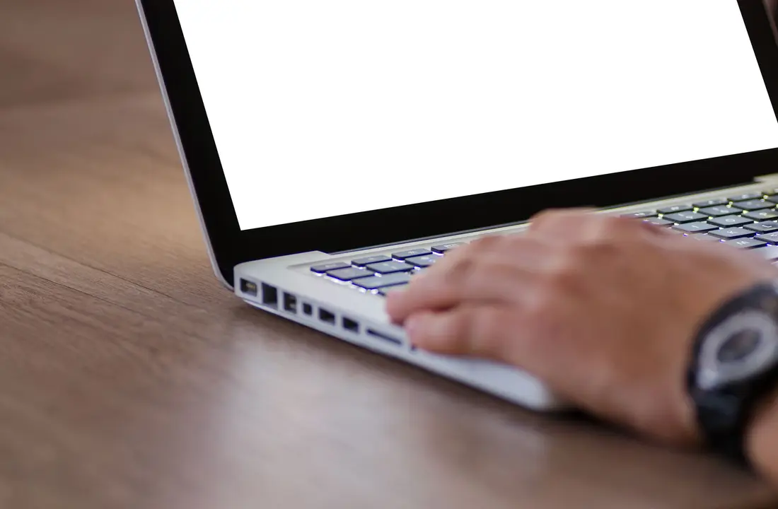 Close-up of a hand using a laptop with a blank screen, ideal for adding custom content.